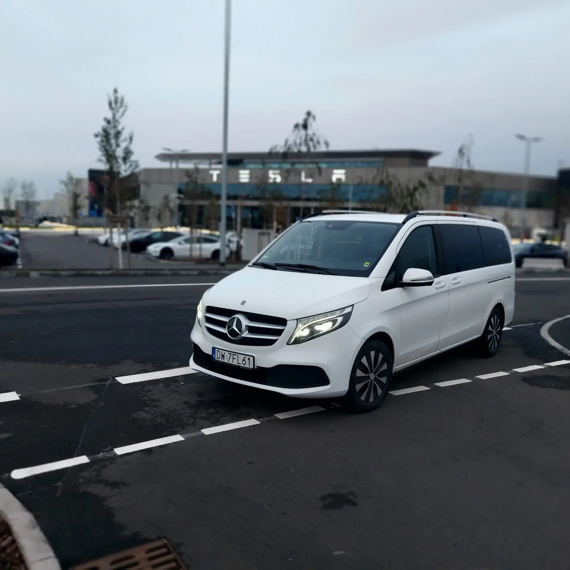 Mercedes na parkingu, w tle oddział firmy Tesla